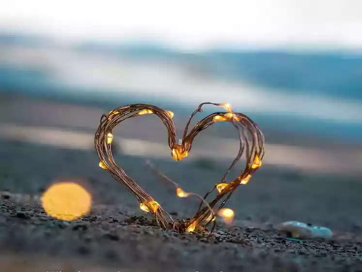 photo représentant un coeur en guirlande lumineuse sur une plage de sable