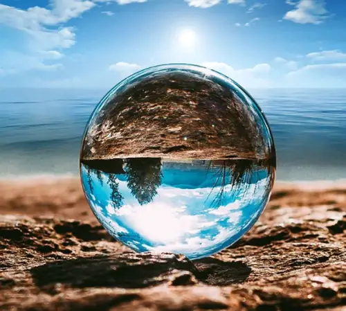 boule de cristal posée sur une plage reflétant le paysage du ciel bleu et du sable