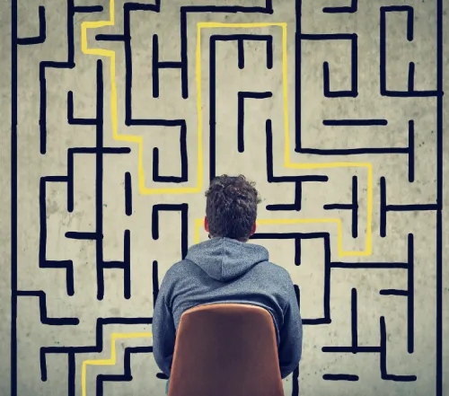 homme assis sur une chaise de dos qui regarde un Labyrinthe dessiné au mur